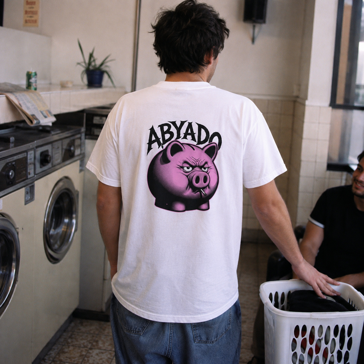 ABYADO Breakage Tee in white, back graphic worn in a laundromat
